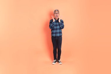 Koyu mavi ekose gömlekli yaşlı bir Asyalı şeftali pembesi bir arka plana karşı duruyor..