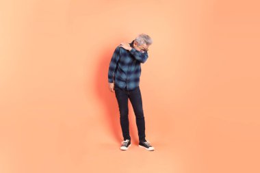 Koyu mavi ekose gömlekli yaşlı bir Asyalı şeftali pembesi bir arka plana karşı duruyor..