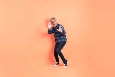 Koyu mavi ekose gömlekli yaşlı bir Asyalı şeftali pembesi bir arka plana karşı duruyor..