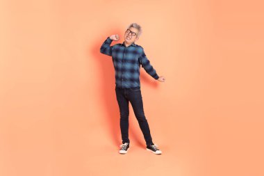 Koyu mavi ekose gömlekli yaşlı bir Asyalı şeftali pembesi bir arka plana karşı duruyor..