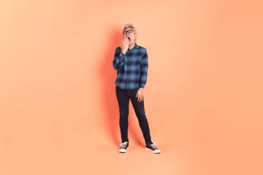 Koyu mavi ekose gömlekli yaşlı bir Asyalı şeftali pembesi bir arka plana karşı duruyor..