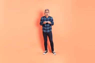 Koyu mavi ekose gömlekli yaşlı bir Asyalı şeftali pembesi bir arka plana karşı duruyor..