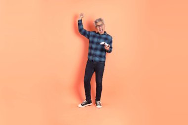 Koyu mavi ekose gömlekli yaşlı bir Asyalı şeftali pembesi bir arka plana karşı duruyor..