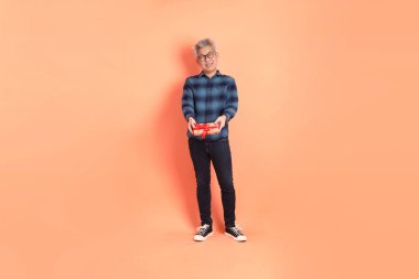 Koyu mavi ekose gömlekli yaşlı bir Asyalı şeftali pembesi bir arka plana karşı duruyor..