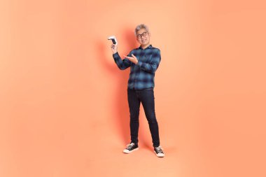 Koyu mavi ekose gömlekli yaşlı bir Asyalı şeftali pembesi bir arka plana karşı duruyor..