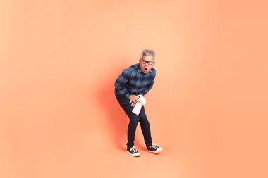 Koyu mavi ekose gömlekli yaşlı bir Asyalı şeftali pembesi bir arka plana karşı duruyor..