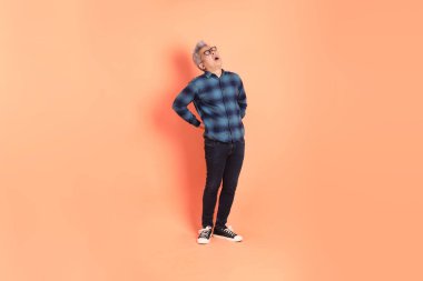 Koyu mavi ekose gömlekli yaşlı bir Asyalı şeftali pembesi bir arka plana karşı duruyor..