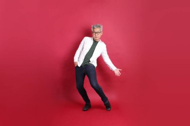 A senior East Asian man in a white shirt stands against a deep red background. clipart