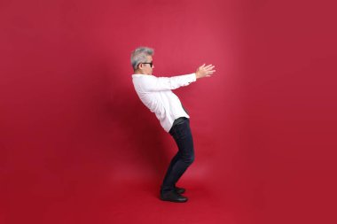 Beyaz tişörtlü üst düzey bir Doğu Asyalı koyu kırmızı arka planda duruyor..