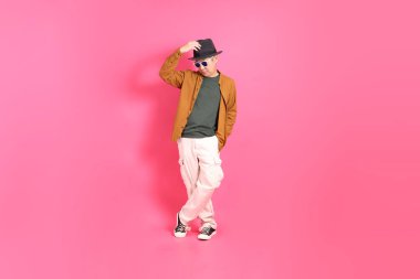 Üst düzey bir Doğu Asyalı, pembe bir arka plana karşı duruyor, renkli bir gömlek giyiyor..