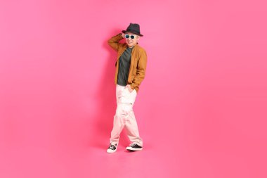 Üst düzey bir Doğu Asyalı, pembe bir arka plana karşı duruyor, renkli bir gömlek giyiyor..