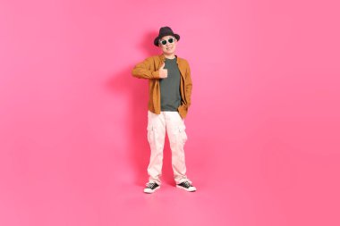 Üst düzey bir Doğu Asyalı, pembe bir arka plana karşı duruyor, renkli bir gömlek giyiyor..