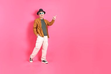 Üst düzey bir Doğu Asyalı, pembe bir arka plana karşı duruyor, renkli bir gömlek giyiyor..