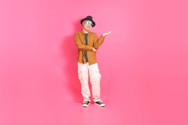 Üst düzey bir Doğu Asyalı, pembe bir arka plana karşı duruyor, renkli bir gömlek giyiyor..