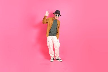 Üst düzey bir Doğu Asyalı, pembe bir arka plana karşı duruyor, renkli bir gömlek giyiyor..