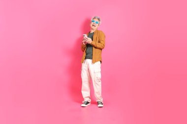 A senior East Asian man stands against a hot pink background, wearing a colorful shirt. clipart