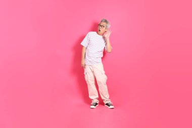 Üst düzey bir Doğu Asyalı seksi pembe bir arka plana karşı duruyor, günlük, renkli bir gömlek giyiyor..