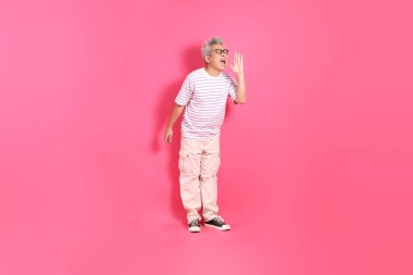 Üst düzey bir Doğu Asyalı seksi pembe bir arka plana karşı duruyor, günlük, renkli bir gömlek giyiyor..