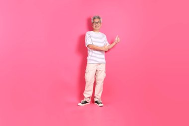 Üst düzey bir Doğu Asyalı seksi pembe bir arka plana karşı duruyor, günlük, renkli bir gömlek giyiyor..