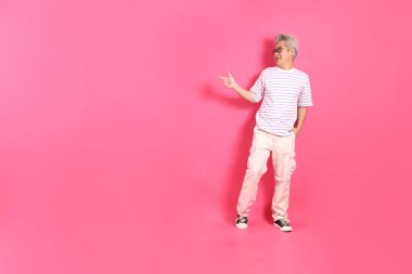 Üst düzey bir Doğu Asyalı seksi pembe bir arka plana karşı duruyor, günlük, renkli bir gömlek giyiyor..