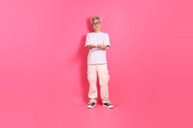 Üst düzey bir Doğu Asyalı seksi pembe bir arka plana karşı duruyor, günlük, renkli bir gömlek giyiyor..