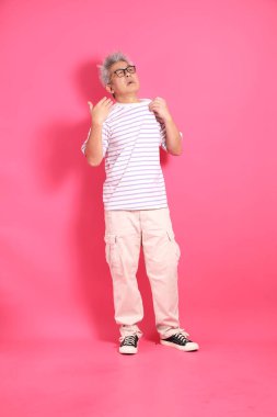 Üst düzey bir Doğu Asyalı seksi pembe bir arka plana karşı duruyor, günlük, renkli bir gömlek giyiyor..