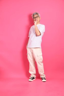 Üst düzey bir Doğu Asyalı seksi pembe bir arka plana karşı duruyor, günlük, renkli bir gömlek giyiyor..