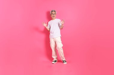 Üst düzey bir Doğu Asyalı seksi pembe bir arka plana karşı duruyor, günlük, renkli bir gömlek giyiyor..