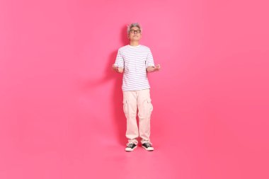 Üst düzey bir Doğu Asyalı seksi pembe bir arka plana karşı duruyor, günlük, renkli bir gömlek giyiyor..