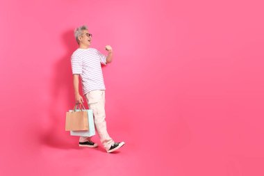 Üst düzey bir Doğu Asyalı seksi pembe bir arka plana karşı duruyor, günlük, renkli bir gömlek giyiyor..