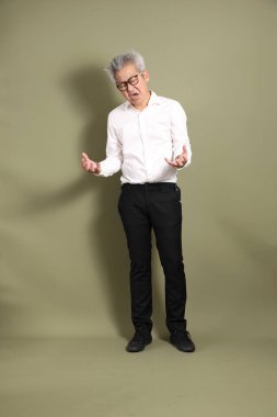 Üst düzey bir Doğu Asyalı işadamı, kıtır beyaz gömlek giymiş koyu yeşil bir arkaplanda duruyor..