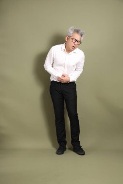 Üst düzey bir Doğu Asyalı işadamı, kıtır beyaz gömlek giymiş koyu yeşil bir arkaplanda duruyor..