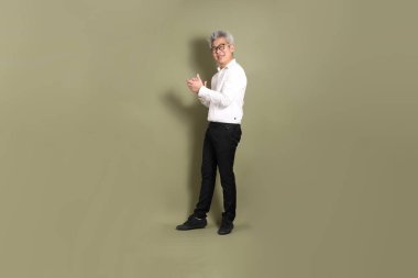 Üst düzey bir Doğu Asyalı işadamı, kıtır beyaz gömlek giymiş koyu yeşil bir arkaplanda duruyor..