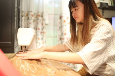 Geceleri elbise dikmek için dikiş makinesi kullanan Doğu Asyalı bir kadın..