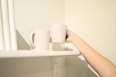 Doğu Asyalı bir kadın kitaplığı beyaz kahve kupalarıyla süslüyor..