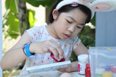 Asyalı bir baba, kızının yaklaşan Paskalya için yumurta boyamasına yardım ediyor..