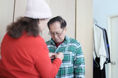 Doğu Asyalı yaşlı bir çift dışarı çıkmak için birbirlerine kışlık giysiler giydiriyorlar.