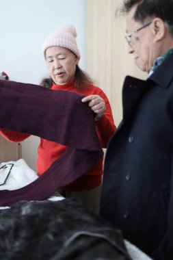 Doğu Asyalı yaşlı bir çift dışarı çıkmak için birbirlerine kışlık giysiler giydiriyorlar.