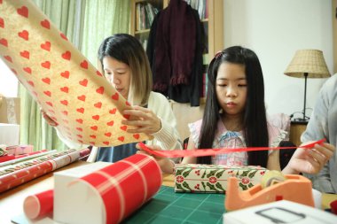 Doğu Asyalı aileler kızlarına yardım ediyor ve yeni yıl hediyelerini nasıl paketleyeceklerini öğretiyorlar..