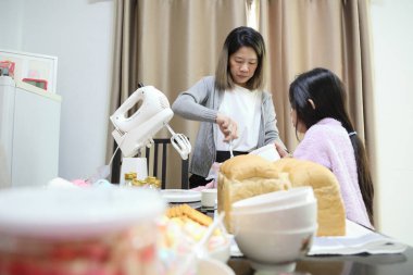 Doğu Asyalı anne yaklaşan parti için kızının yardımıyla ev ekmeğini pişiriyor ve dekore ediyor..