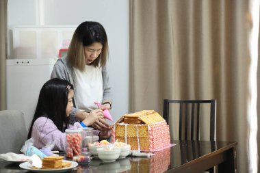 Doğu Asyalı anne yaklaşan parti için kızının yardımıyla ev ekmeğini pişiriyor ve dekore ediyor..