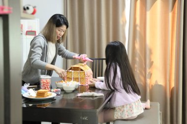 Doğu Asyalı anne yaklaşan parti için kızının yardımıyla ev ekmeğini pişiriyor ve dekore ediyor..