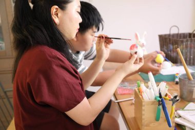 The East Asian single mother and her son are painting eggs for the upcoming Easter. clipart