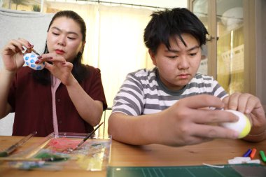 The East Asian single mother and her son are painting eggs for the upcoming Easter. clipart