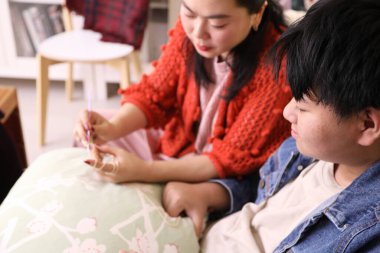 Asyalı anne oğluna oturma odasında örgü örmeyi öğretiyor..