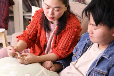 Asyalı anne oğluna oturma odasında örgü örmeyi öğretiyor..