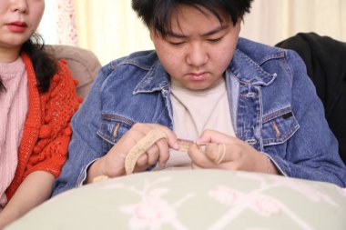 Asyalı anne oğluna oturma odasında örgü örmeyi öğretiyor..
