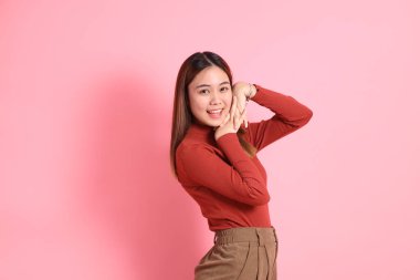 Gündelik giysiler içinde pembe arka planda duran genç Güneydoğu Asyalı kadın..