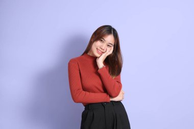 Mor arka planda dikilen, günlük giysiler içindeki genç Güneydoğu Asyalı kadın..