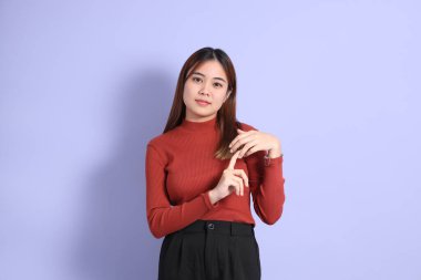 Mor arka planda dikilen, günlük giysiler içindeki genç Güneydoğu Asyalı kadın..